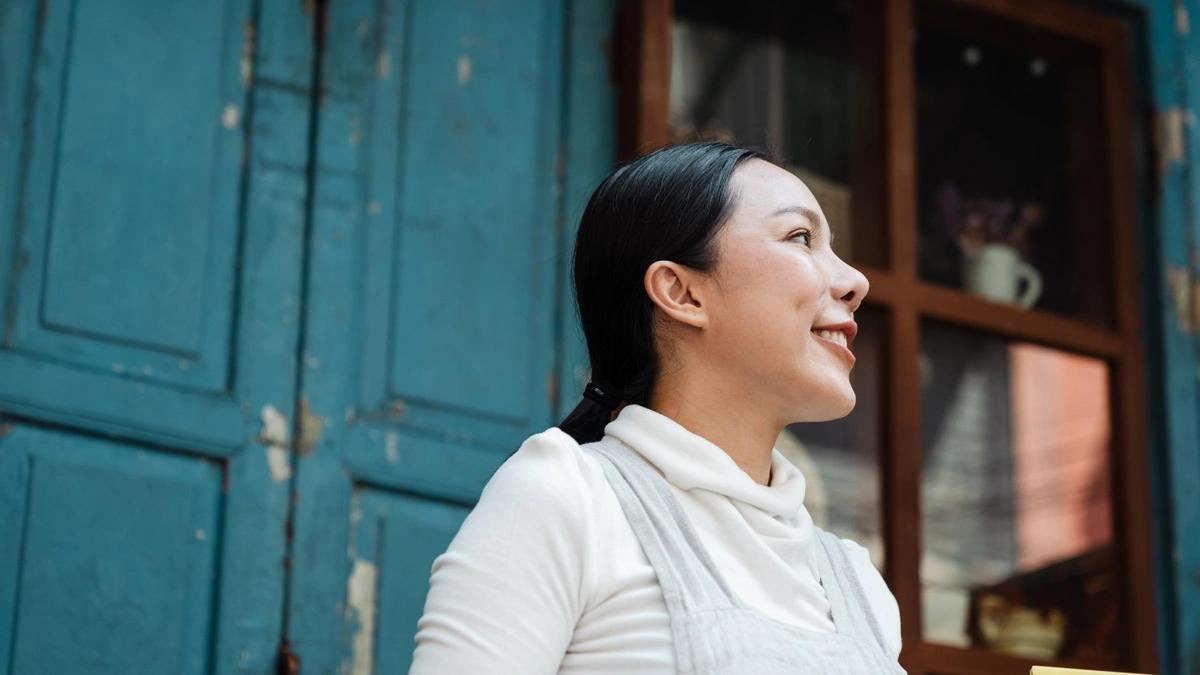 Portrait, girl looks to her left and smiles, with a blue wall in the background.