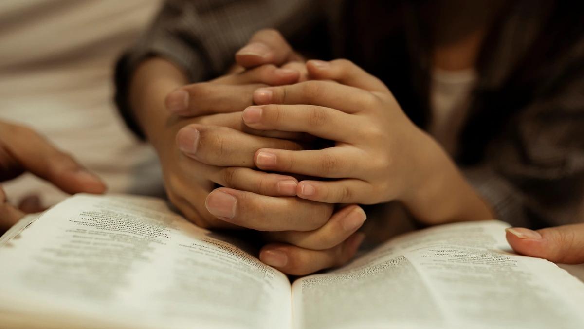 parent and children's hands folded together on a bible close up