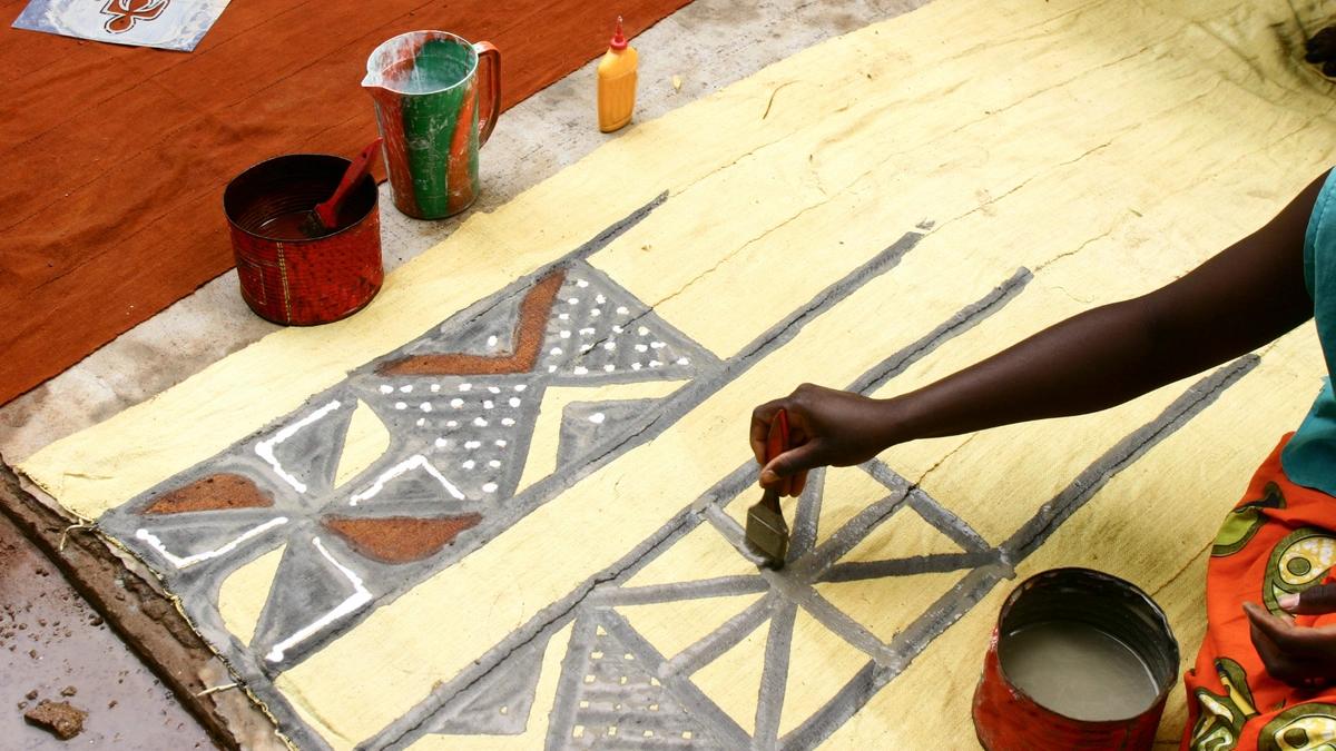 A woman sits on the floor painting a design onto fabric