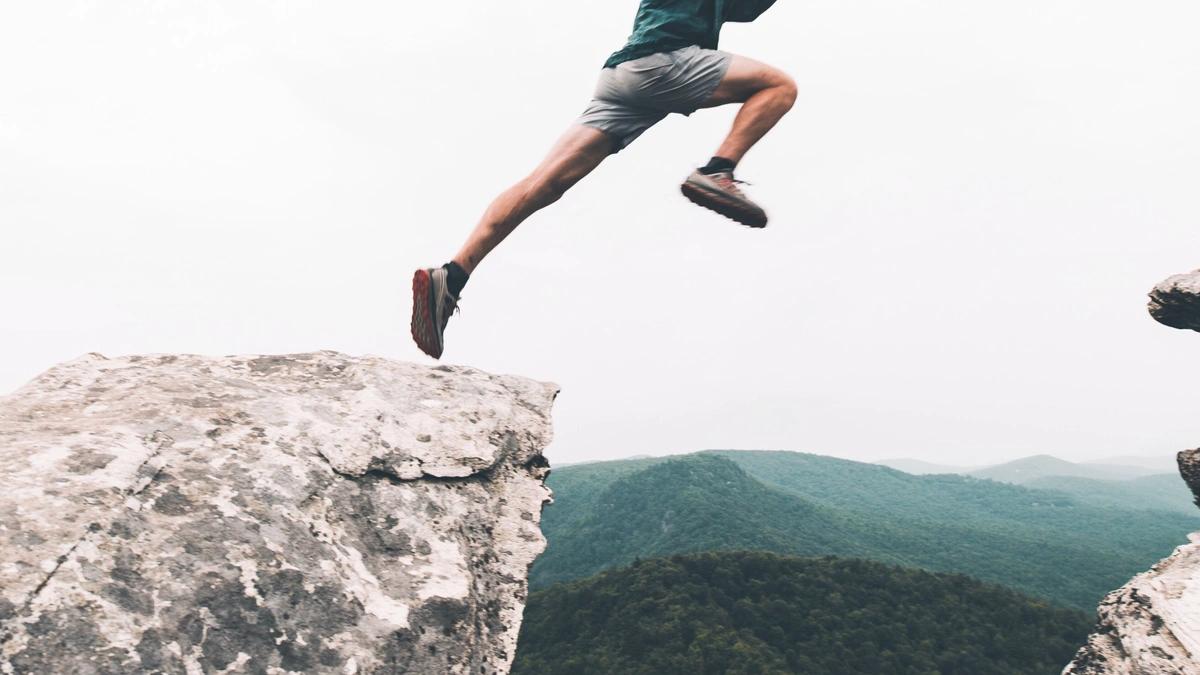 waist down shot of man jumping from rock to rock with rolling hills/mountains and horizon in the background