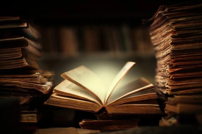 glowing open book in dark room with stacks of books