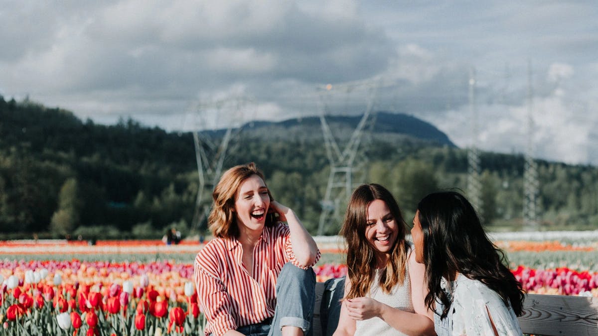 three women laughing on a bench in a tulip field